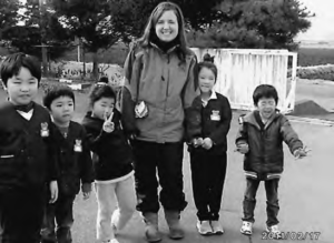 photograph of a young woman with several young children, smiling and holding hands