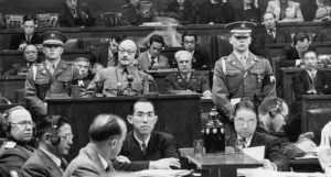men in military garb stand behind podiums, wearing headphones as they listen in to the trials.