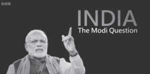 Image of a man holding out his finger with the background writing The Modi Question