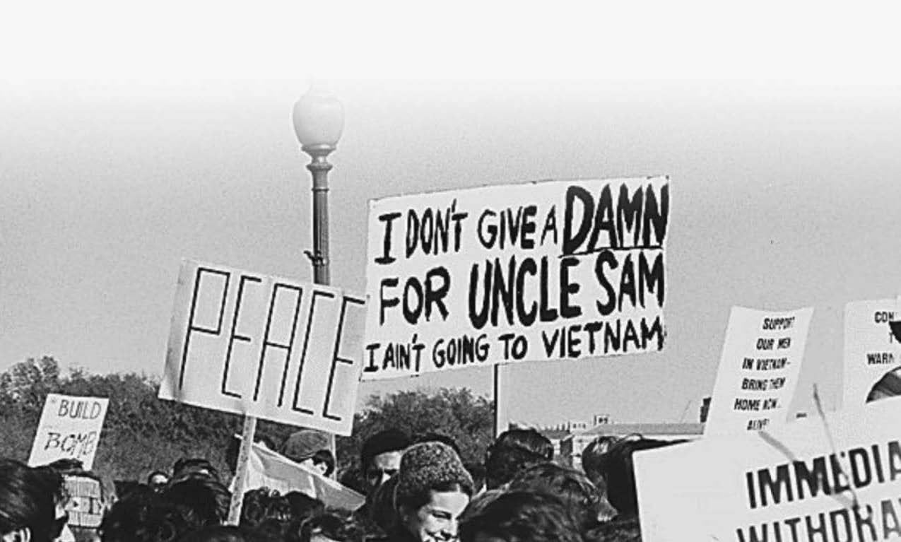 black and white photo of protest signs that read "peace" and "I don't give a damn for uncle sam I ain't going to Vietnam"