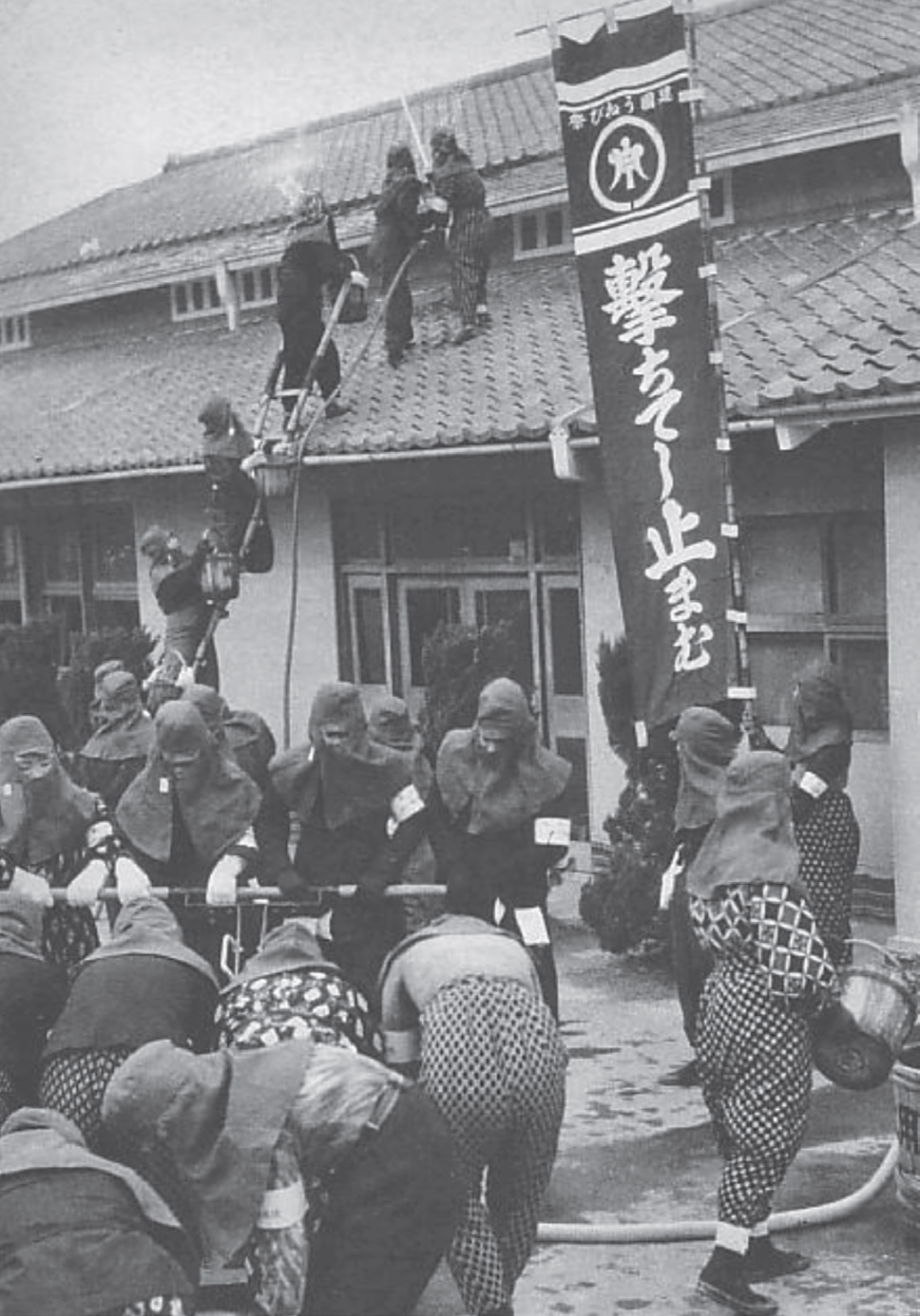 photo of people wearing hoods shooting water at a house and holding a banner