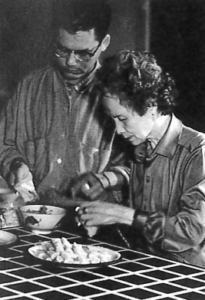Photo of one man and an old woman preparing spring rolls standing side on the table