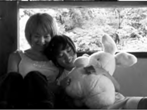 Screenshot of two girls sitting against each other, holding a plush rabbit in hand