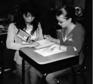 The photo shows a woman talking to another woman and pointing her finger at the paper