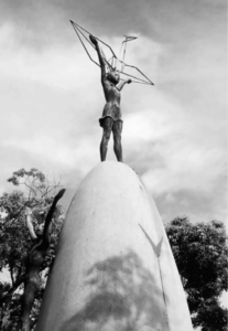 A statue of a girl standing on an oval stone with a model of an origami crane held high in her hands